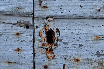 Antique keyhole plate with traces of rust covered with white paint on a wooden door