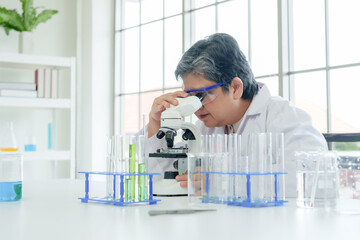 Senior Asian female science teacher, Experienced lab worker in white uniform examines sample under...