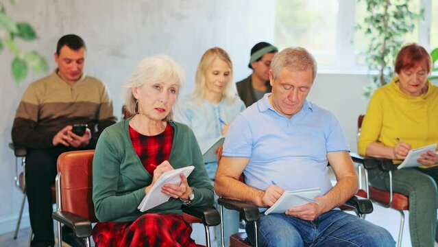 Positive interested elderly people listening attentively and taking notes on lesson during language courses for older adults
