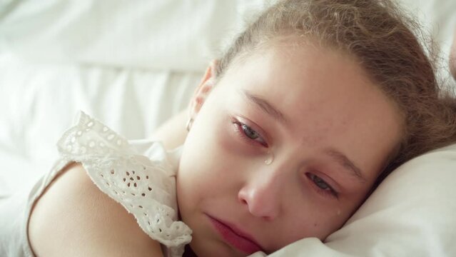 Mom takes pity on her daughter. Portrait upset child little girl with big tears flowing down his cheeks,child lies at home on bed next to his mother and cries, tears flow with a screaming face.