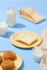 Morning meal concept with few types of bread displayed on ceramic dishes with cups and a bottle of milk. Blue surface. The concept of delicious and healthy food