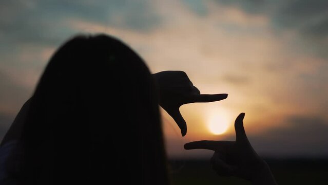 Happy girl figure frame from fingers.figure with hands is symbol of dreams and freedom. girl dream.Girl outdoors in park silhouette at sunset.Figure frame fingers hand figure in nature.freedom concept
