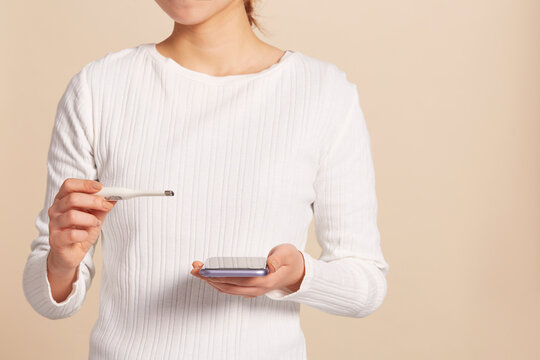 体温計とスマートフォンを持った女性