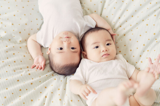 布団の上に寝転ぶ双子の赤ちゃん