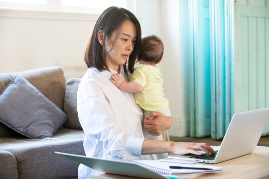 赤ちゃんを抱っこしながらパソコンで仕事をしている女性
