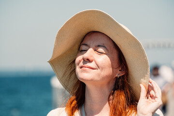 A red-haired woman enjoys a serene moment, eyes closed, with the sun on her face