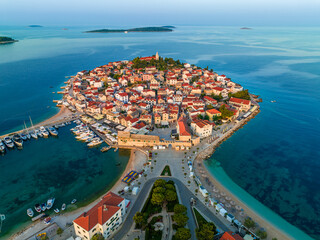 Primosten, Croatia - Aerial view of old town of Primosten peninsula, St. George's Church on a sunny summer morning in Dalmatia, Croatia. Blue and mooring yachts at sunrise on the Adriatic sea coast - obrazy, fototapety, plakaty
