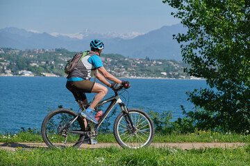 A man on a mountain bike in motion with Lake Garda in the background, mountain peaks in the snow.