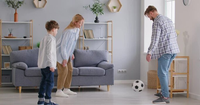Happy smiling young parents playing football game with their child boy son in the living room at home enjoying spending time together. Family leisure concept. 4k video. Slow motion video.