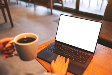 Mockup image of a woman using and working on laptop computer with blank white desktop screen while drinking coffee