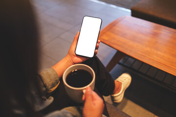 Mockup image of a woman holding mobile phone with blank desktop screen while drinking coffee in cafe - 791325411