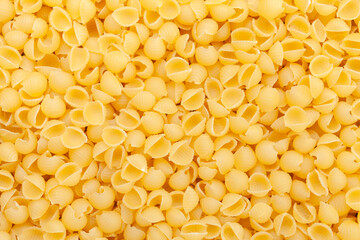 Uncooked, yellow shell pasta background. Top view