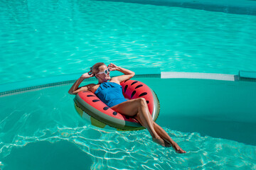 Happy woman in a swimsuit and sunglasses floating on an inflatable ring in the form of a...