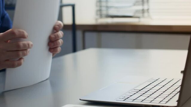 Close-up tilting shot of male office employee in suit, with slicked back hair, in glasses opening laptop, putting presentation pages on table, propping chin and glaring across at annoying colleagueClo