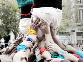 Detail of the base of a human tower of castellers with colorful handkerchiefs. Raised hands of the castellers forming the pinya (base) and supporting the tower