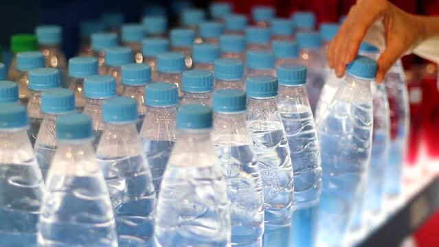 Rows of clear plastic Bottles with Water and Female hand takes one. Woman choosing a mineral water in store. Healthy lifestyle concept