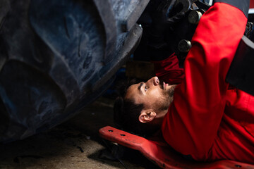 Experienced caucasian mechanic working under the tractor repairing agricultural machinery.