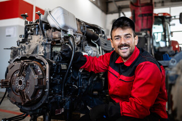 Portrait of mechanic servicing tractor engine in workshop.