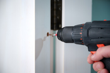 Construction worker with a screwdriver installing a door. Accessories for assembling, install furniture, repair home. Man dressed in work attire, helmet and protective glasses. Home renovation concept