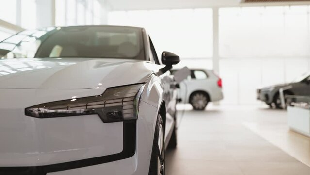 Front part of brand new modern white car, parked at showroom. Reflection in led headlights of luxury vehicle in dealership.
