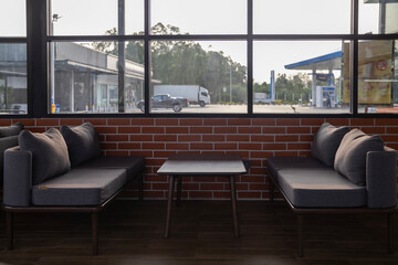 Set of sofas and wooden tables inside a coffee shop next to a gas station.