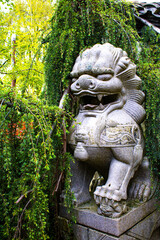 Fototapeta na wymiar Guardian of the Garden: Stone Lion Statue Amidst Verdant Foliage