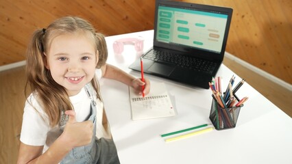 Little pretty caucasian girl doing classwork while showing a thumb up gesture. Young child writing...