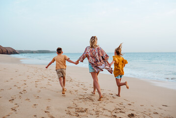 Mother with two kids on beach. Young family enjoying sandy beach in Canary Islands. Concept of beach summer vacation with kids.