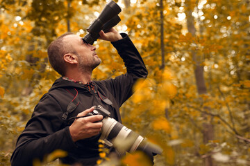 Man using binoculars and camera for birdwatching and other observing animals in nature.