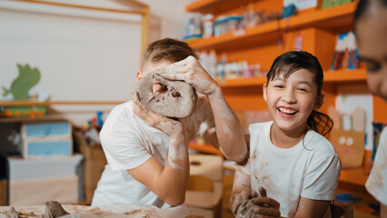Smart boy pick clay while looking though hole at pottery workshop.Skilled diverse highschool student working and modeling dough while laugh at happy child at art lesson. Creative art. Edification.
