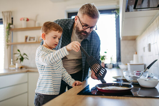 Boy helping father to make pancake. Father spending time with son at home, making snack together, cooking. Fathers day concept.