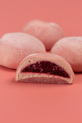 Traditional Japanese dessert, mochi cake in thin pink rice dough on a pink background with pink filling, cut, open space
