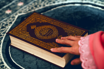 The hand of a woman in prayer clothes holds the Quran on the prayer cloth.