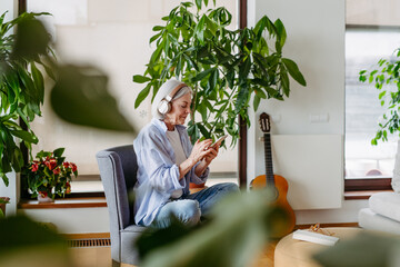 Older woman with headphones on head, listening music, relaxing at home.