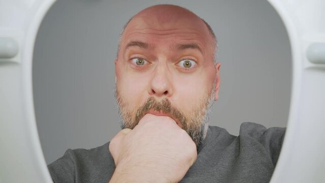 Man opening toilet lid and vomiting at home. Male vomits at restroom, looking sick and illness. Nausea and vomiting as symptom of gastroenteritis. View from toilet bottom. Cleanliness and hygiene