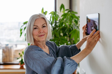Mature woman adjusting household functions, lighting, security cameras, door locks, smart thermostat or heating settings. Sustainable and smart technology at home.