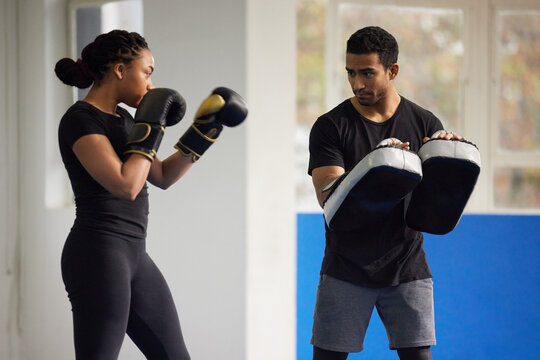 Self defence, woman and trainer with boxing gloves for fight workout of muay thai exercise. Fitness coach, athlete and sport pads for strength and power training in a gym with cardio and instructor