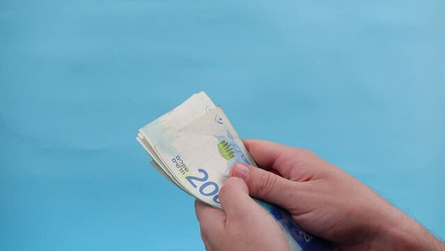 Hands of a person counting and waving Israel currency &ndash; New Israeli shekel (NIS) in denominations of 200 shekels banknotes, as a concept of rising prices, economic crisis, and wealth.