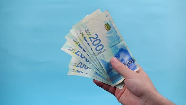 Hands of a person counting and waving Israel currency &ndash; New Israeli shekel (NIS) in denominations of 200 shekels banknotes, as a concept of rising prices, economic crisis, and wealth.