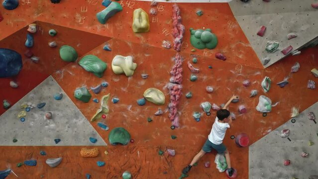 A strong and hardy little boy of 10 years old trains on a climbing wall indoors. Endurance and purposefulness training in young children. High quality 4k footage