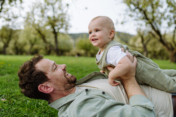 Father lying and playing with little baby, having fun in grass during warm spring day. Father's day concept.