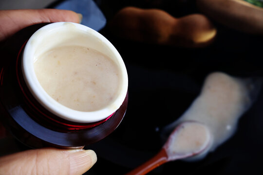 Light brown cream jar sideways Put the spoon on the black surface. Next is the ripe tamarind fruit.

