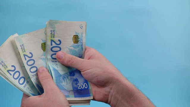 Hands of a person counting and waving Israel currency &ndash; New Israeli shekel (NIS) in denominations of 200 shekels banknotes, as a concept of rising prices, economic crisis, and wealth.