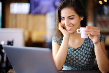 Happy woman checking laptop and drinking coffee in a bar - 791380692