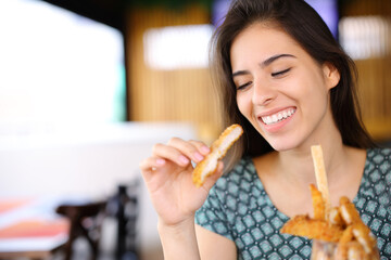 Happy woman eating chicken fingers alone in a restaurant