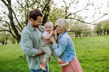 New parents holding small toddler, baby, outdoors in spring nature. Older First-time parents.