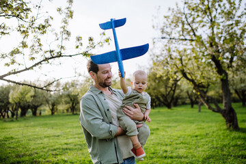 Father and toddler playing with foam glider plane. Single dad having fun with baby during warm spring day. Father's day concept.