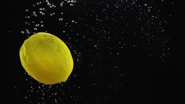 Lemon dropping or falling in clear water with bubbles over black background, copy space for promotional text
