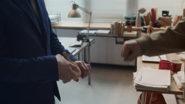 Medium close-up shot of two unrecognizable rival corporate workers doing reconciliatory handshake, man in suit clasping wooden toy hand, then both bumping fistsMedium close-up shot of two unrecognizab