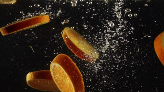 Fresh oranges slices falling deeply under water with big splash isolated over black background